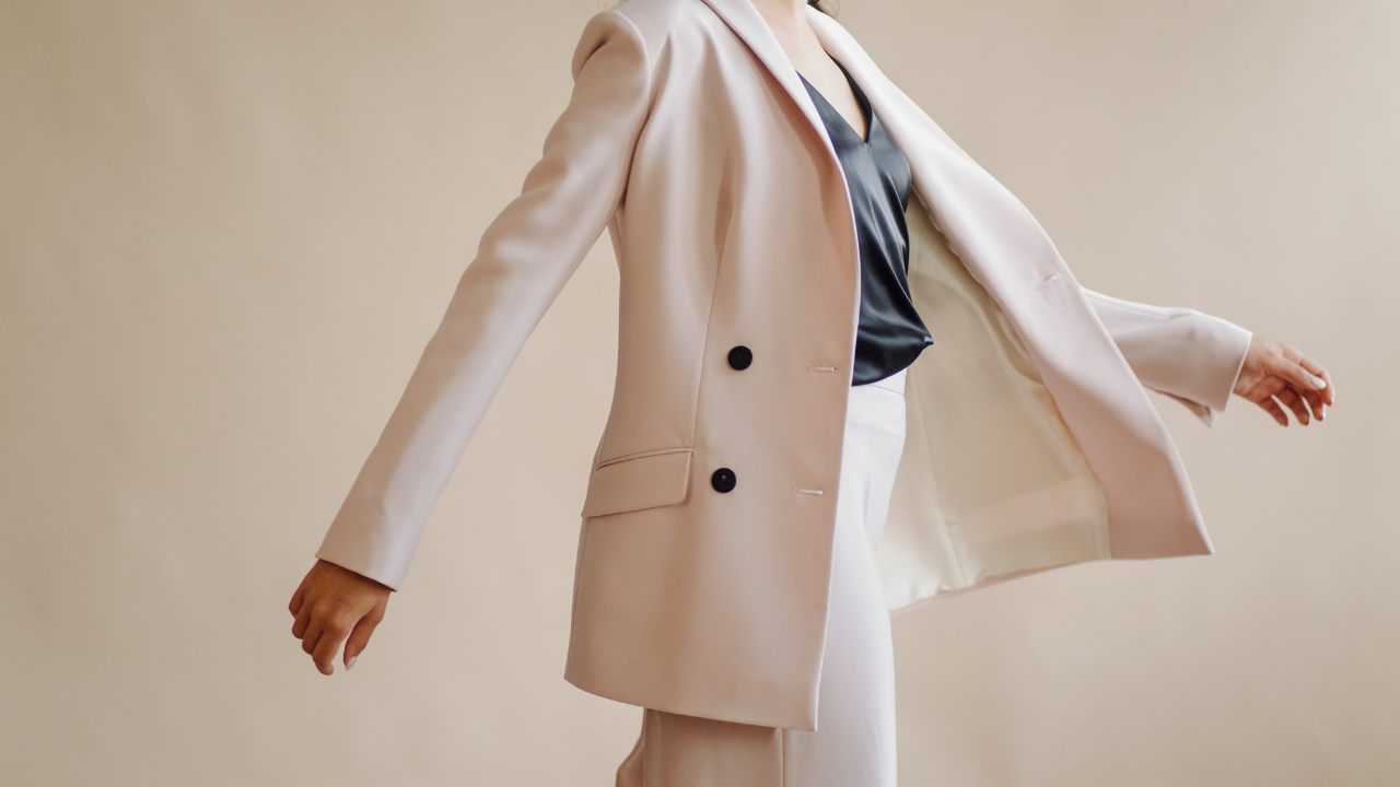 Person wearing a light-colored suit jacket and pants with a dark top, channeling French style against a plain beige background.